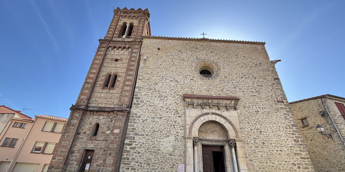 Facciata esterna in pietra della Chiesa di Santa Maria (Église Sainte-Marie) a Le Boulou con il suo antico campanile e il portale romanico.