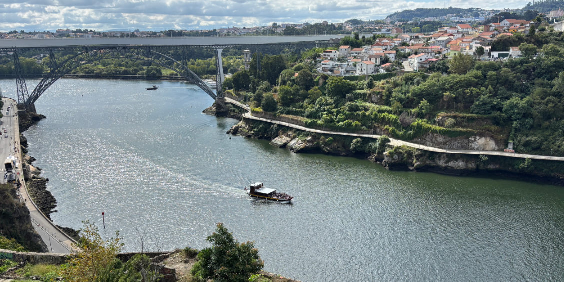 Battello turistico in navigazione sul fiume Douro a Porto con vista sui ponti e le rive scoscese.