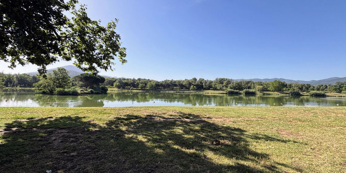 Uno dei laghi di Saint-Jean-Pla-de-Corts nei Pirenei Orientali, circondato da prati verdi e boschi sotto un cielo azzurro.