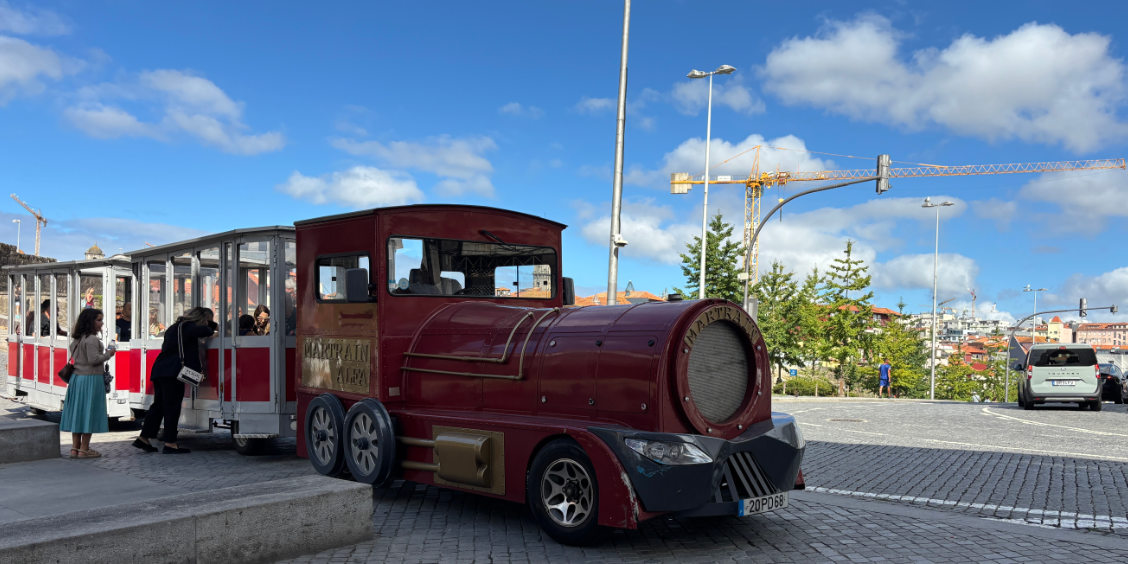 Trenino turistico su gomma fermo in una piazza panoramica di Porto con passeggeri a bordo.