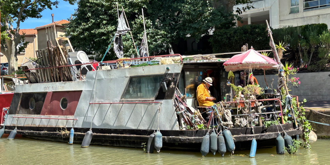 Caratteristica casa-barca (péniche) ricca di dettagli ormeggiata lungo il Canal de la Robine a Narbona, Francia.