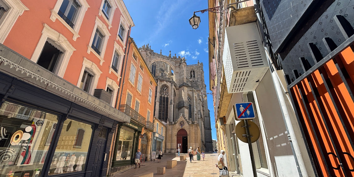 Scorcio di una via pedonale nel centro storico di Narbona con la monumentale Cattedrale di San Giusto e San Pastore sullo sfondo.