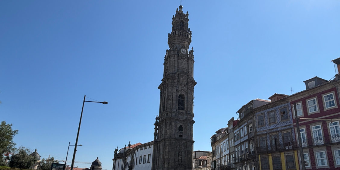 Torre dos Clérigos a Porto vista dal piano strada tra gli edifici storici e cielo azzurro.